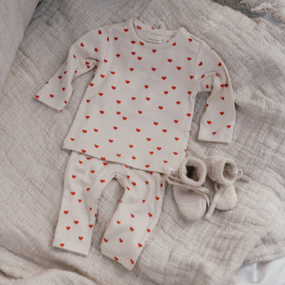 Een babypakje in gebroken wit met rode hartjes en ivory kleurige babysokjes