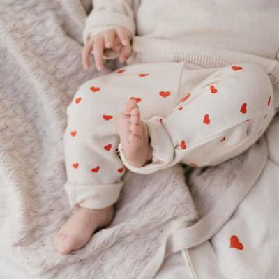 Een baby in een gebroken wit overslagshirtje met een gebroken wit broekje met rode hartjes