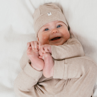 Een baby met een beige mutsje en een beige baby trui en een beige baby broekje