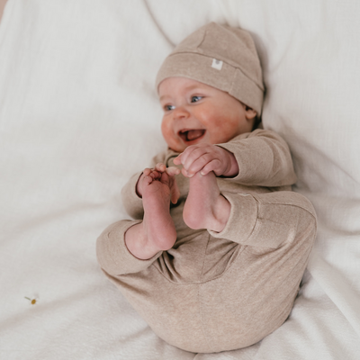 Een baby in een beige mutsje en een beige broekje en een beige overslagromper