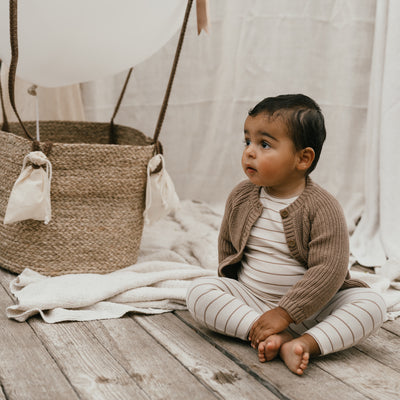 Een baby met een bruin vestje met een gestreepte longsleeve en een gestreept babybroekje