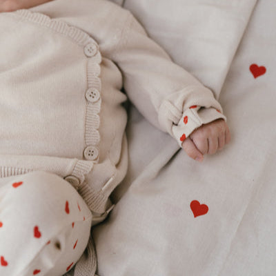 Een baby in een gebroken wit overslagshirtje met een gebroken wit broekje met rode hartjes