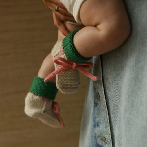 Hvid babyslofjes gemaakt van 100% merinowol in de kleur cream met groen en een roze vetertje.