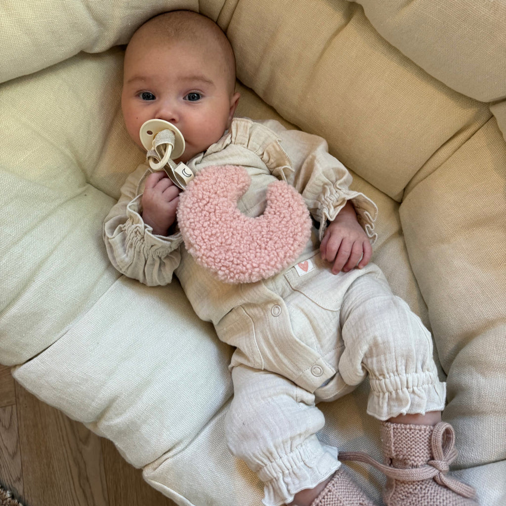 Een baby met een speentje en een licht roze speenknuffel in de vorm van een maantje