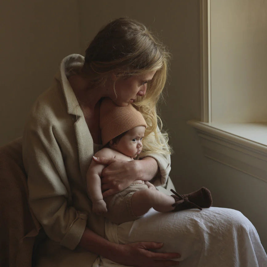 Een moeder met een baby in een kort beige babybroekje