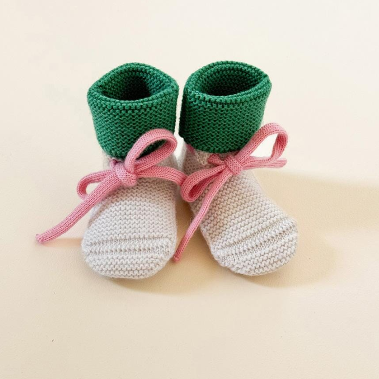 Hvid babyslofjes gemaakt van 100% merinowol in de kleur cream met groen en een roze vetertje.