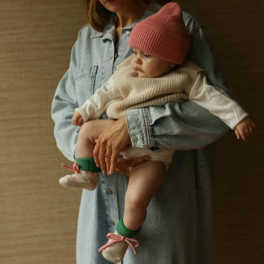 Hvid babyslofjes gemaakt van 100% merinowol in de kleur cream met groen en een roze vetertje.