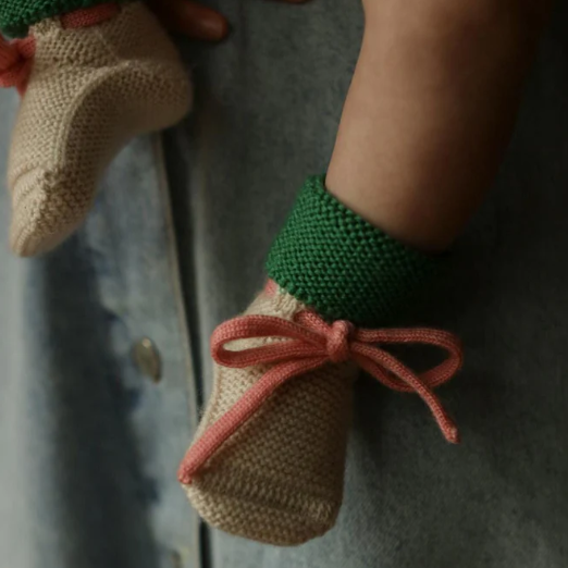 Hvid babyslofjes gemaakt van 100% merinowol in de kleur cream met groen en een roze vetertje.