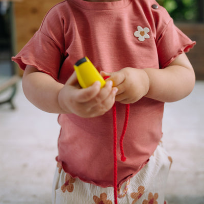 Een meisje in een roze t-shirtje met wit broekje met beige bloemetjes