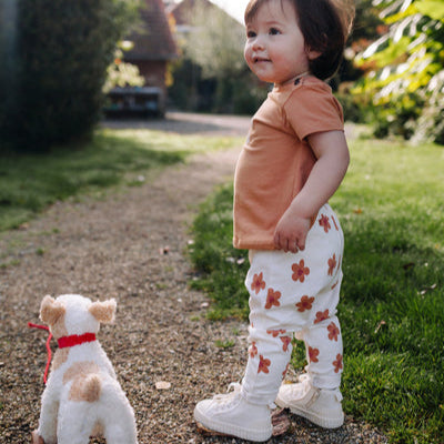 Een meisje in een lange witte broek met beige bloemetjes en een beige t-shirt