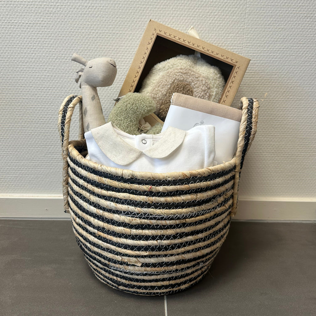 Een beige gevulde kraammand met muziekmobiel, knuffel, rammelaar, speenknuffeltje, grote hydrofiele beige doek en een prachtig beige, wit boxpakje.