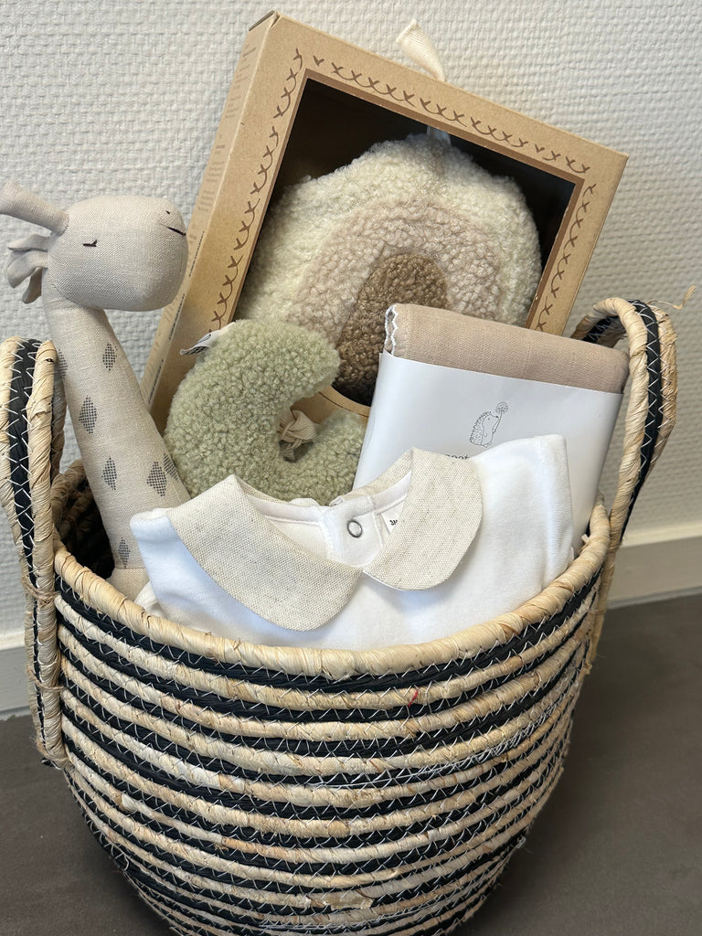 Een beige gevulde kraammand met muziekmobiel, knuffel, rammelaar, speenknuffeltje, grote hydrofiele beige doek en een prachtig beige, wit boxpakje.