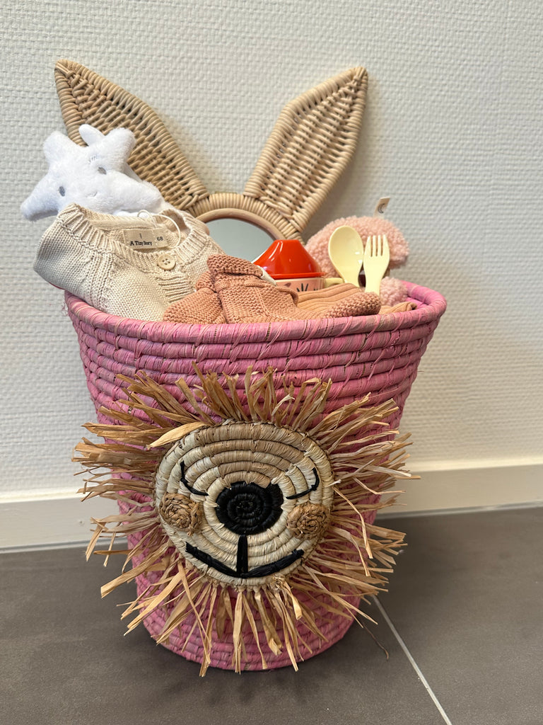 Grote roze kraammand met een roton spiegel van een konijn, wit knuffeldoekje, setje kleding, speenknuffeltje, baby bestek, tuitbeker en babyslofjes.