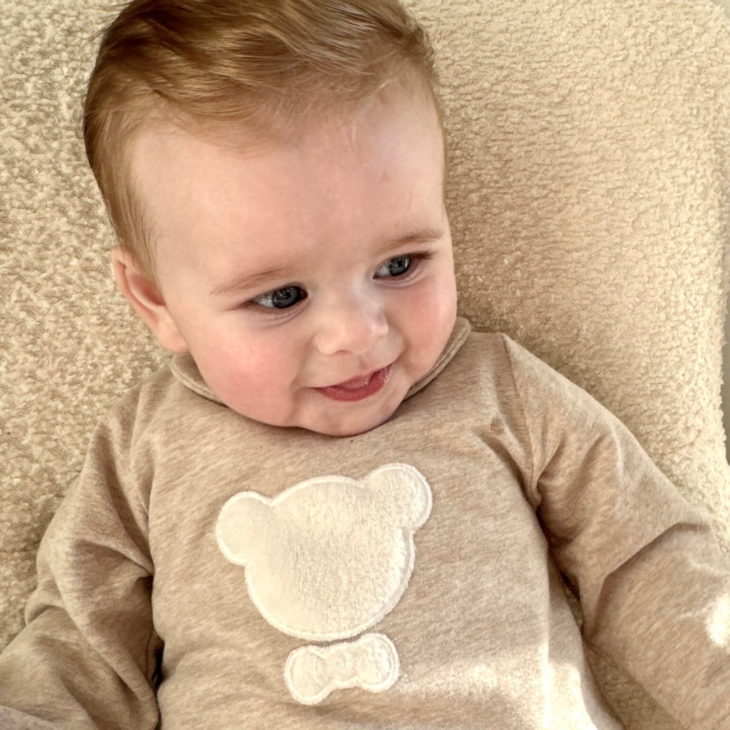 Een kindje in een beige boxpakje met een witte beer 