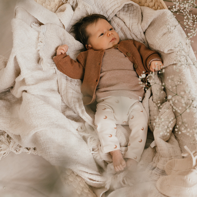 Een kindje met een bruin vestje, beige long sleeve en een broekje met maantjes