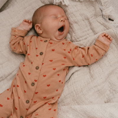 Een baby in een koraalkleurig boxpakje met rode hartjes