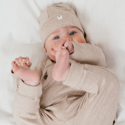 Een kindje met een beige mutsje, beige long sleeve met overslag en een beige broekje