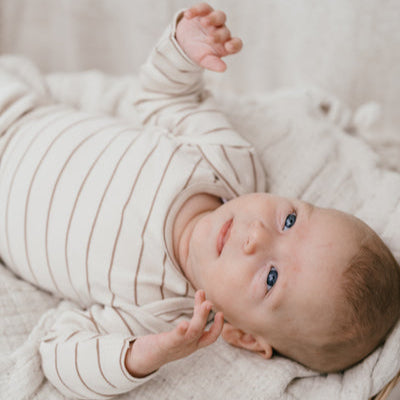 Een babytje die een beige longsleeve met streepjes draagt