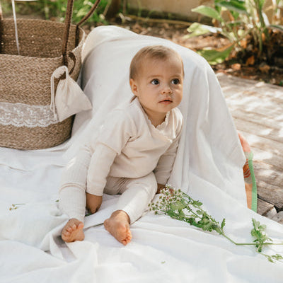 Een baby in een gebroken wit overslagshirtje en een gebroken wit broekje