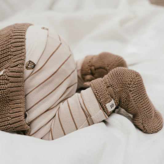 Een baby met een gestreept broekje, karamelkleurig vestje en karamelkleurige babysokjes