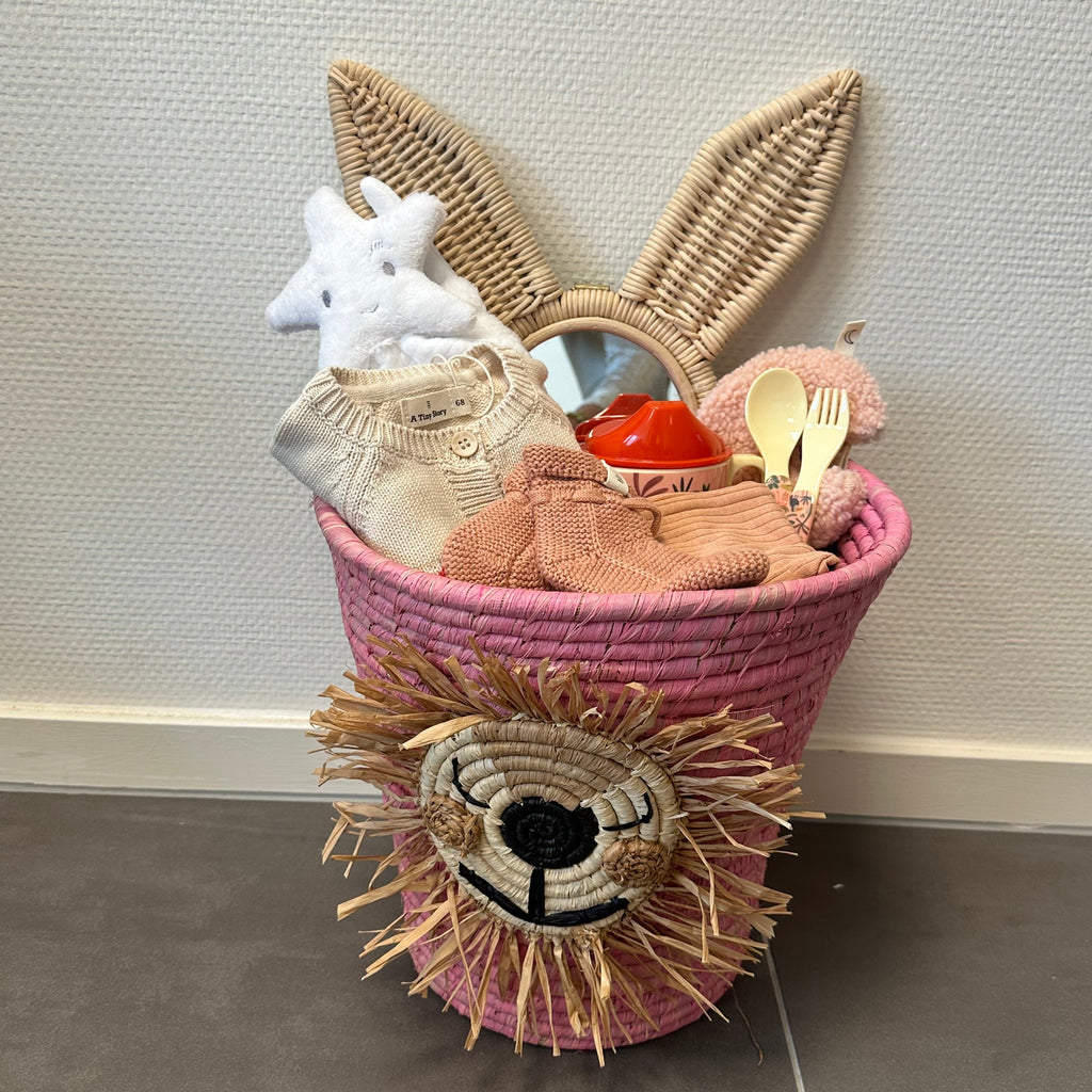 Grote roze kraammand met een roton spiegel van een konijn, wit knuffeldoekje, setje kleding, speenknuffeltje, baby bestek, tuitbeker en babyslofjes.