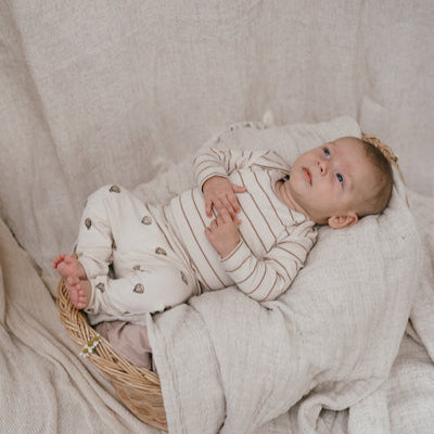 Een baby in een gebroken wit shirtje met streepjes en een gebroken wit broekje met luchtballonnen
