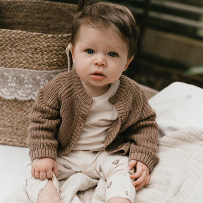 Een jongetje in een bruin vestje met ivory kleurige longsleeve en een gebroken wit broekje met luchtballonnen. 