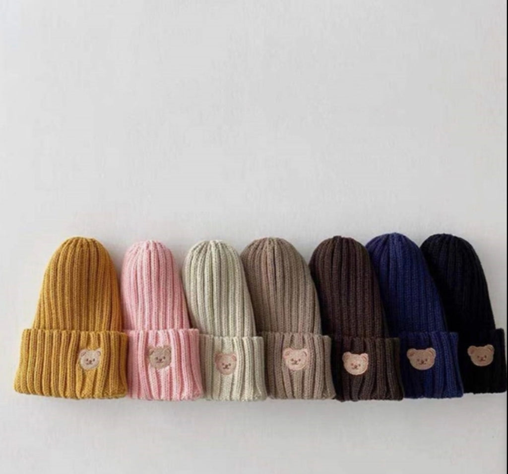 Verschillende kleuren mutsen met een geborduurd beertje op een rijtje.