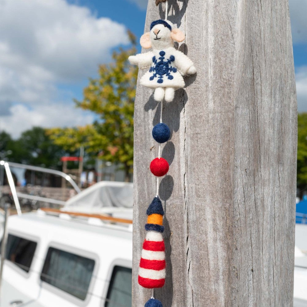 Handgemaakte slinger van wolvilt met nautische elementen. Eem vuurtoren, zeilbootje, anker, reddingsboei, stuurwiel.
