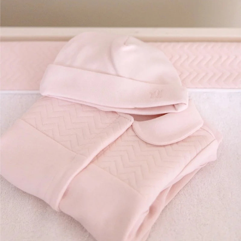 Een licht roze boxpakje met een licht roze babymutsje