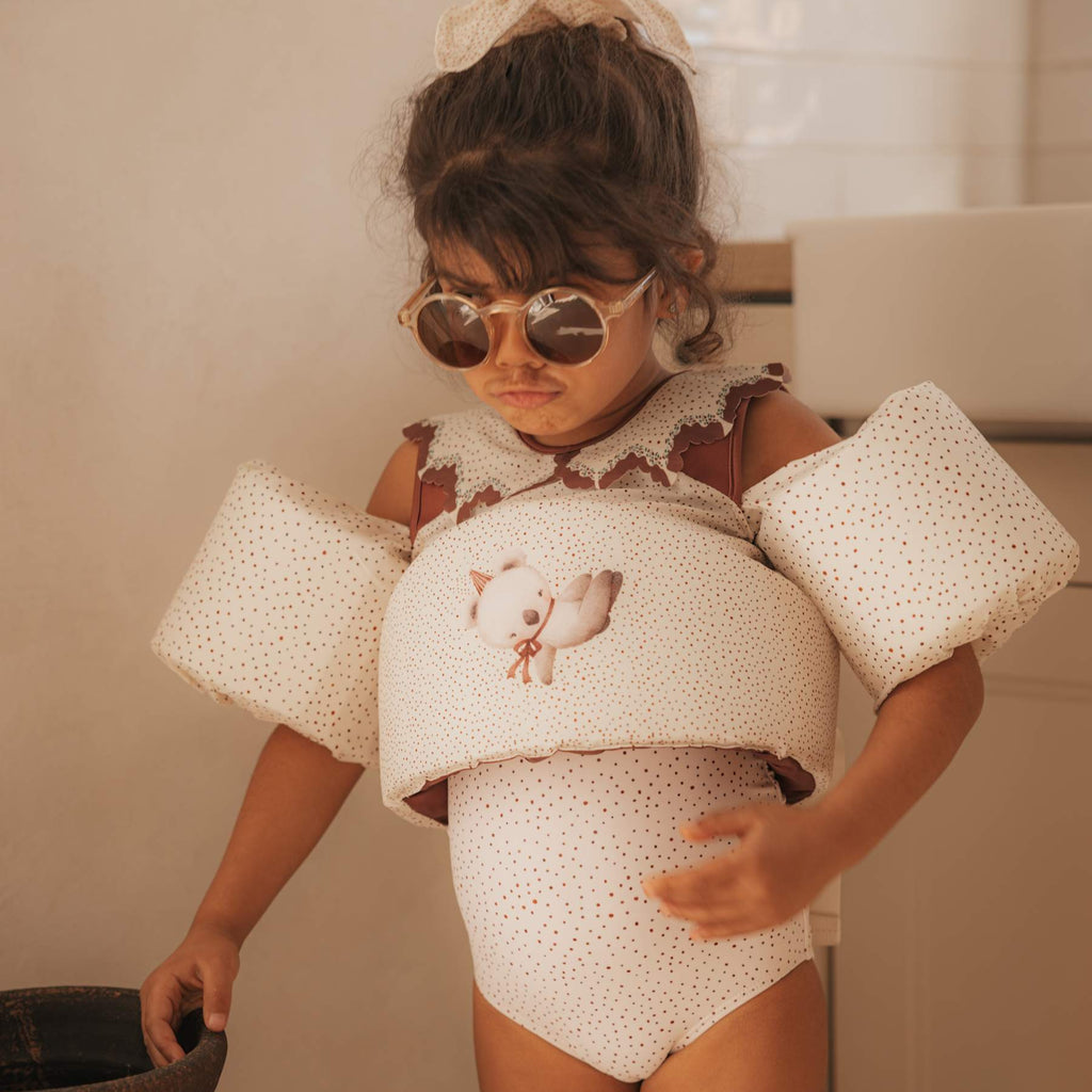 Een meisje met een zonnebril in zwemkleding met een zwemvestje 