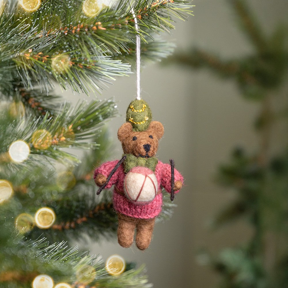 Een kerstboomhanger in de vorm van een beertje met een trommel in zijn hand. In de kleur cyclaam, groen en wit.