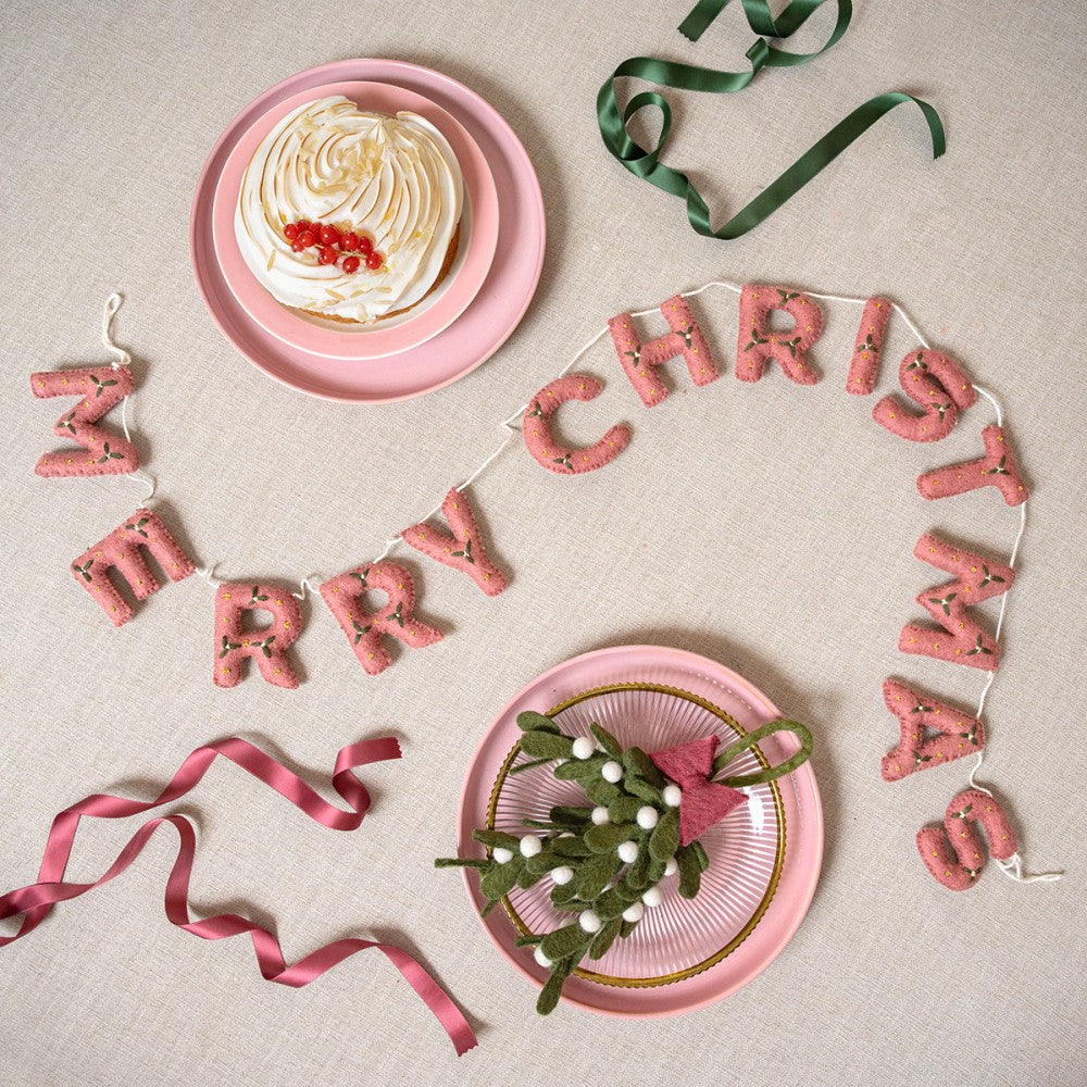 Een mooie slinger met de letter Merry Chirstmas gemaakt van wolvilt in de kleur oud roze met kleine mistletoe versiering.