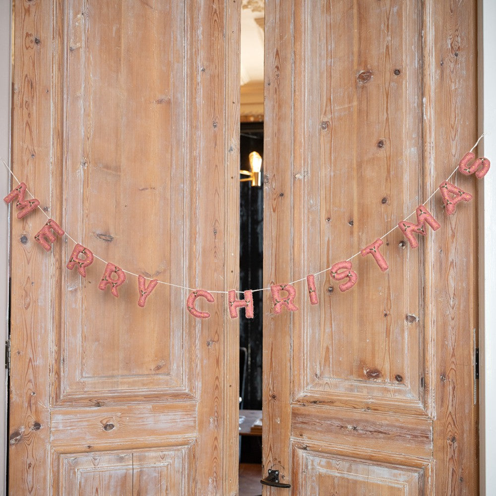 Een mooie slinger met de letter Merry Chirstmas gemaakt van wolvilt in de kleur oud roze met kleine mistletoe versiering.