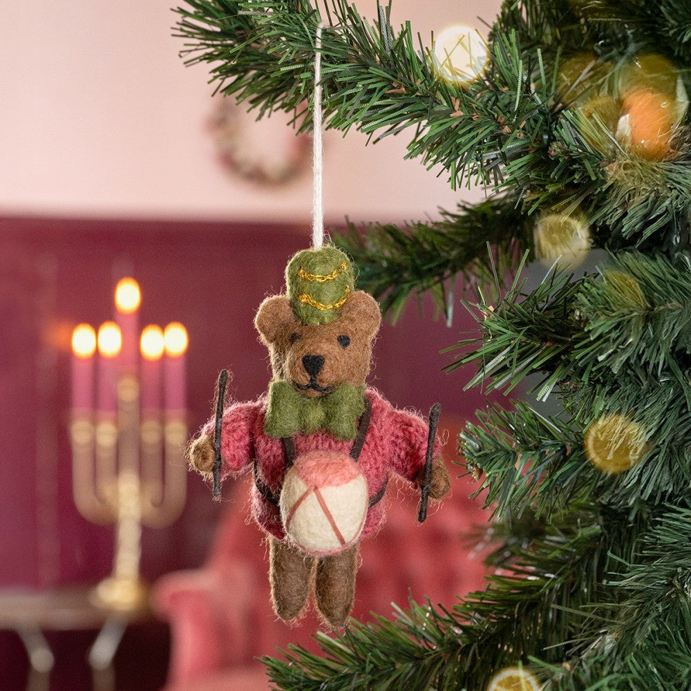 Een kerstboomhanger in de vorm van een beertje met een trommel in zijn hand. In de kleur cyclaam, groen en wit.