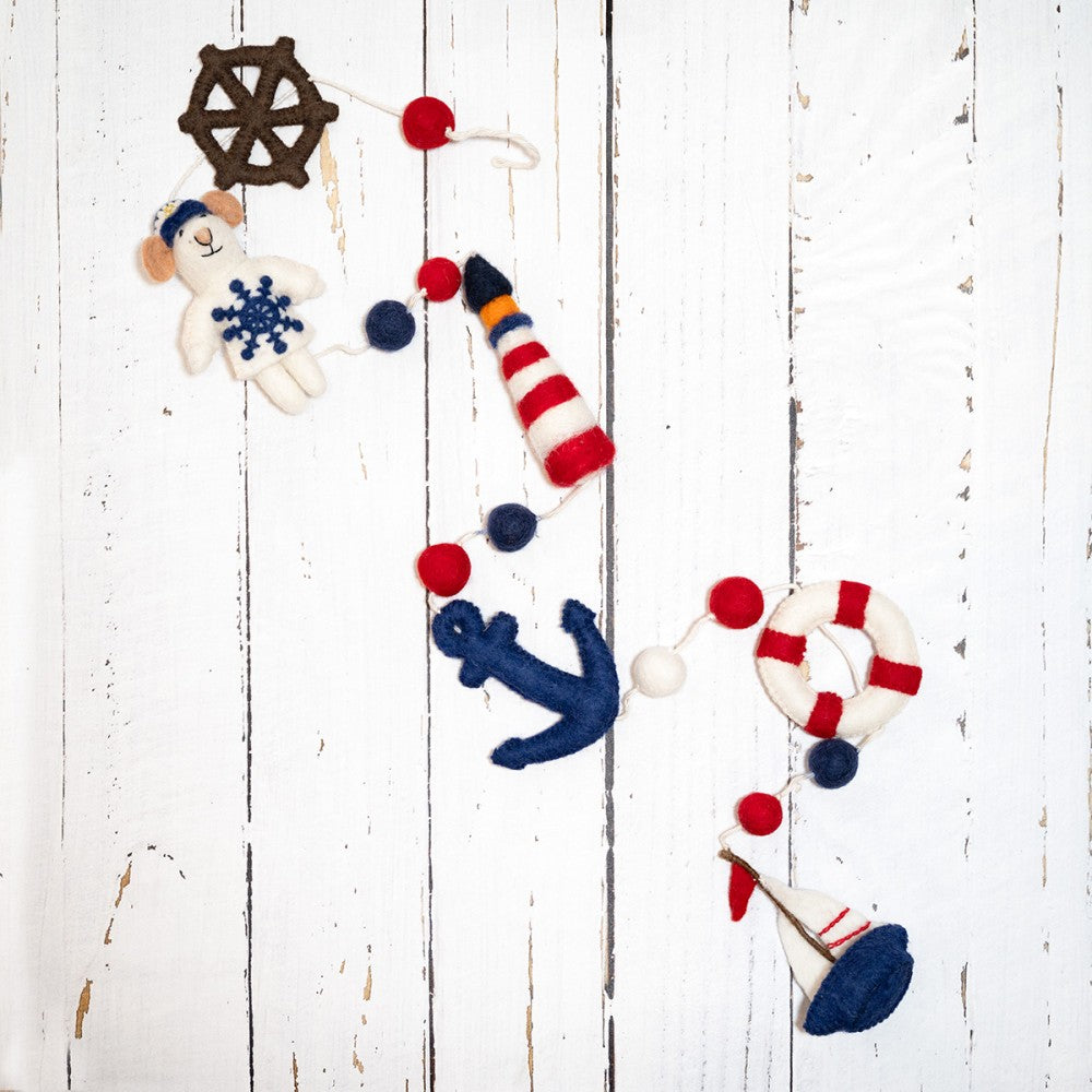 Handgemaakte slinger van wolvilt met nautische elementen. Eem vuurtoren, zeilbootje, anker, reddingsboei, stuurwiel.
