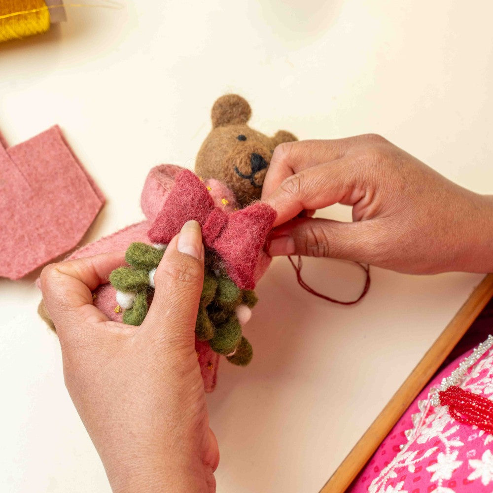 Bruine beer gemaakt van wolvilt in een roze jurk met een bosje Mistletoe in haar handjes.