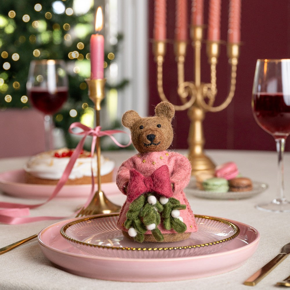 Bruine beer gemaakt van wolvilt in een roze jurk met een bosje Mistletoe in haar handjes.