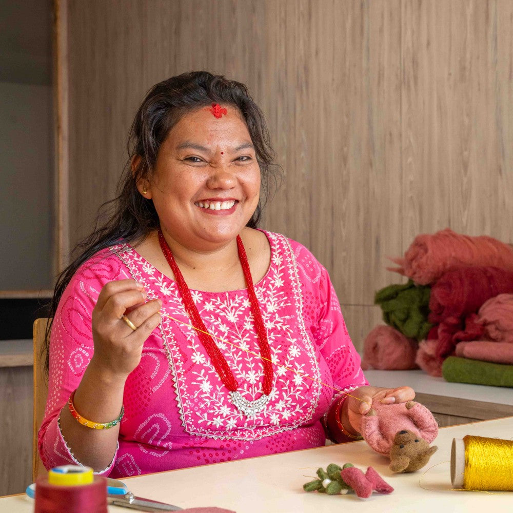 Bruine beer gemaakt van wolvilt in een roze jurk met een bosje Mistletoe in haar handjes.