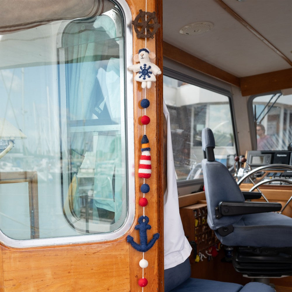 Handgemaakte slinger van wolvilt met nautische elementen. Eem vuurtoren, zeilbootje, anker, reddingsboei, stuurwiel.