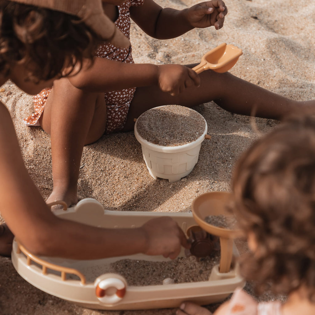Kinderen spelen in het zand met schepjes, emmertjes en een bootje