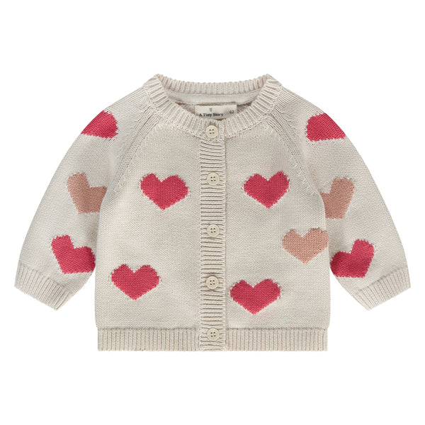 Een gebroken wit babyvestje met rode en koraalkleurige hartjes