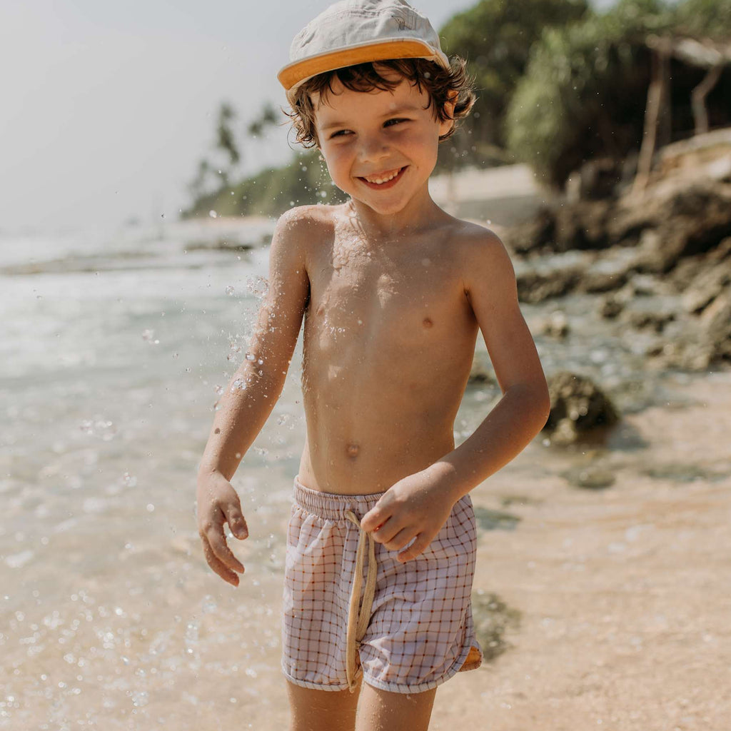 Een jongetje op het strand in een licht geruite zwembroek