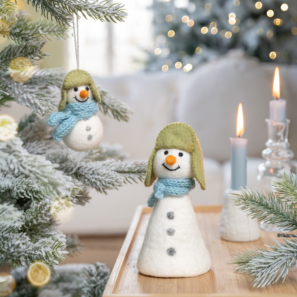 Een sneeuwpop met een groene muts en een blauwe sjaal gemaakt van wolvilt.