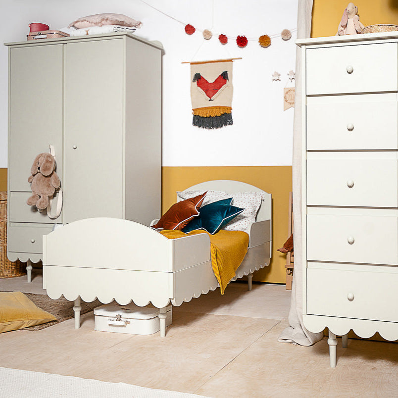 Een kinderkamer met een kledingkast, peuterbed en hoge commode kast.