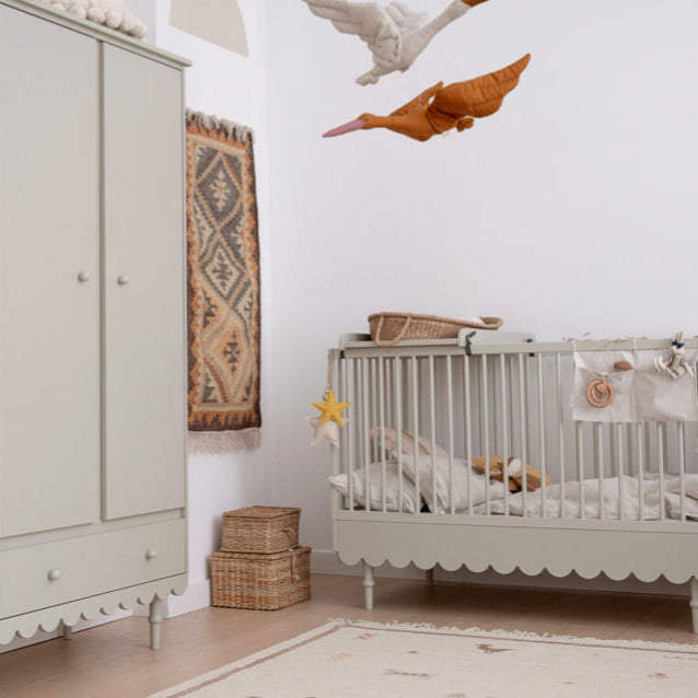 Een olijfgroene ledikant in een kinderkamer met een commode opzetstuk